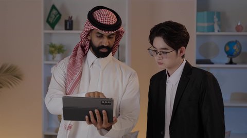 تبادل الخبرات والمعرفة بين البلاد, عقد اتفاقيات عمل جديدة، استضافة رجال الاعمال الاجانب في المملكة العربية السعودية, رجل عربي خليجي سعودي يرتدي الزي التقليدي مع شاب صيني يرتدي البدلة الرسمية يقومان بالعمل على التابليت المحمول