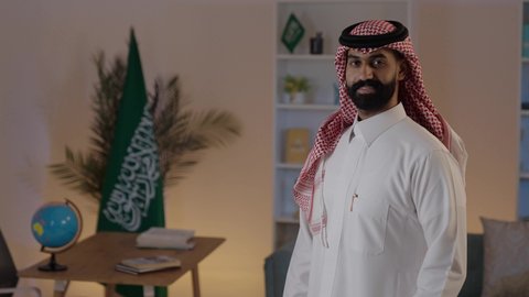 الوقوف باستقامة والنظر إلى الكاميرا بإيماءات السعادة والسرو، رجل عربي خليجي سعودي يرتدي الثوب والشماغ التقليدي ، مفهوم الاناقة والاهتمام بالمظهر الخارجي
