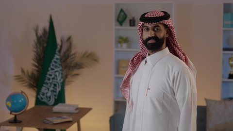 Standing upright and looking at the camera with gestures of happiness and joy, an Arab Gulf Saudi man wearing the traditional thobe and ghutrah, a concept of elegance and attention to external appearance.