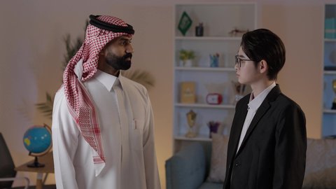 الوقوف بأيدي متقاطعة والنظر إلى الكاميرا بايماءات السعادة والسرور، استضافة رجال الاعمال الاجانب في المملكة العربية السعودية، تبادل الخبرات والمعرفة بين البلاد، رجل عربي خليجي سعودي يرتدي الزي التقليدي يقف مع شاب صيني يرتدي البدلة الرسمية