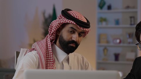 عقد اتفاقيات عمل جديدة، استضافة رجال الاعمال الاجانب في المملكة العربية السعودية, تبادل الخبرات والمعرفة بين البلاد, رجل عربي خليجي سعودي يرتدي الزي التقليدي مع شاب صيني يرتدي البدلة الرسمية يقومان بالعمل على اللابتوب المحمول