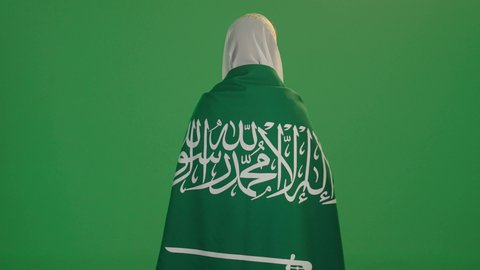 التباهي بإنجازات البلاد, بورتريه من الخلف لامرأة عربية خليجية سعودية مبتسمة ترتدي الشيلة والنشل تحمل علم يوم تأسيس الدولة السعودية الأولى 1727 م، ارتداء أزياء المنطقة الشرقية، يوم بدينا 22 فبراير، الاحتفال بالأعياد الوطنية, خلفية خضراء, كروما