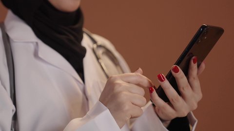 إعداد التقارير الطبية, بورتريه مقرب ليد طبيبة عربية خليجية سعودية  تقوم بتسجيل معلومات المرضى باستخدام الهاتف, تقديم الخدمات العلاجية في المراكز الطبية, خلفيه بنية