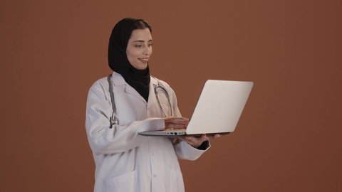 دمج التقنيات الحديثة بالمجالات الطبية, تطور القطاع الصحي، بورتريه من الجانب لطبيبة عربية خليجية سعودية ترتدي المعطف الأبيض و السماعة تقوم بتقديم الاستشارات للمرضى باستخدام الحاسوب، خلفية بنية