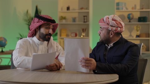 التفاهم والتعاون بين الزملاء لتحقيق أهداف الشركة، التحقق والتدقيق في العروض المالية، تطوير خطة وآلية العمل، رجل عربي خليجي سعودي يرتدي الزي التقليدي والشماغ يقوم بشرح المهام لزميله، كتابة وتسجيل الملاحظات, إنجاز الأعمال المكتبية
