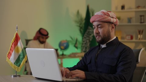موظف سعودي يعمل على جهاز التابلت، إدارة شؤون الأعمال وتنظيمها عبر الاجهزة التقنية، دمج العمل مع التقنية والتكنولوجيا، تصفح مواقع التواصل الاجتماعي، رجل اعمال عربي خليجي سعودي يرتدي الزي التقليدي والشماغ  يعمل على جهاز اللابتوب بإيماءات التركيز