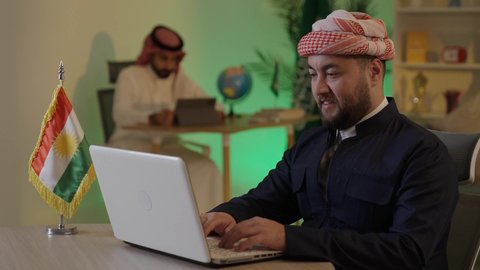 دمج العمل مع التقنية والتكنولوجيا، إدارة شؤون الأعمال وتنظيمها عبر الاجهزة التقنية، تصفح مواقع التواصل الاجتماعي، رجل اعمال عربي خليجي سعودي يرتدي الزي التقليدي والشماغ  يعمل على جهاز اللابتوب بإيماءات التركيز، موظف سعودي يعمل على جهاز التابلت