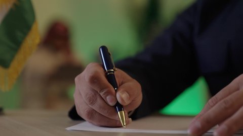 Achieving the company's goals, completing office tasks, verifying and auditing financial offers, developing a work plan and mechanism, an Arab Gulf Saudi man wearing casual attire and a shemagh is writing and recording notes, a Saudi employee working on a laptop.