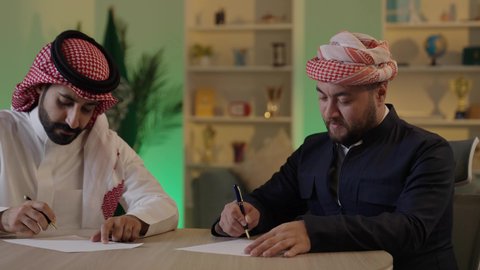 كتابة وتسجيل الملاحظات, إنجاز الأعمال المكتبية، التفاهم والتعاون بين الزملاء لتحقيق أهداف الشركة، التحقق والتدقيق في العروض المالية، تطوير خطة وآلية العمل، رجل عربي خليجي سعودي يرتدي الزي التقليدي والشماغ يقوم بشرح المهام لزميله