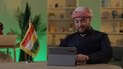 تصفح مواقع التواصل الاجتماعي، إدارة شؤون الأعمال وتنظيمها عبر الاجهزة التقنية، دمج العمل مع التقنية والتكنولوجيا، رجل اعمال عربي خليجي سعودي يرتدي الزي  الكاجوال والشماغ  يعمل على جهاز التابلت بإيماءات التركيز