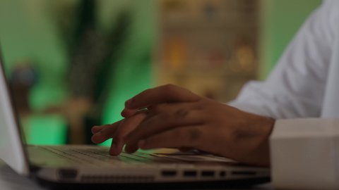 اجراء اجتماع عمل عن بعد ،  إدارة شؤون الأعمال وتنظيمها عبر الاجهزة التقنية، دمج العمل مع التقنية والتكنولوجيا، تصفح مواقع التواصل الاجتماعي، رجل اعمال عربي خليجي سعودي يرتدي الزي التقليدي والشماغ  يعمل على جهاز الحاسوب المحمول بإيماءات التركيز