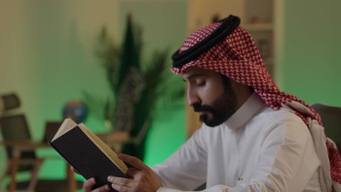 The role of education in the development of Saudi society, the importance of reading in expanding the horizons of knowledge and increasing information, an Arab Gulf Saudi man wearing traditional attire and a shemagh sitting on a comfortable sofa reading from a book, knowledge is the key to development and success.