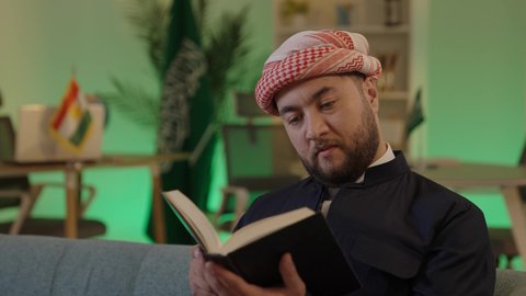 دور التعليم في تطوير المجتمع السعودي، أهمية القراءة في توسيع آفاق المعرفة وزيادة المعلومات، رجل عربي خليجي سعودي يرتدي الزي الكاجوال والشماغ يجلس على اريكة مريحة يقرأ من كتاب، العلم مفتاح التطور والنجاح