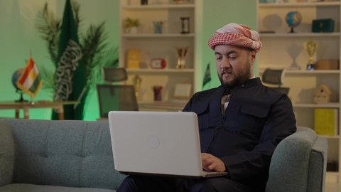 استخدام التقنيات الحديثة ، إدارة شؤون الأعمال وتنظيمها عبر الاجهزة التقنية، دمج العمل مع التقنية والتكنولوجيا، تصفح مواقع التواصل الاجتماعي، رجل اعمال عربي خليجي سعودي يرتدي الزي الكاجوال والشماغ  يعمل على جهاز الحاسوب المحمول بإيماءات التركيز