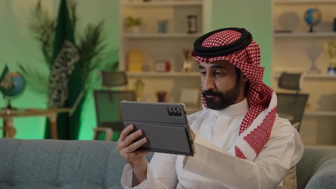 تصفح مواقع التواصل الاجتماعي، إدارة شؤون الأعمال وتنظيمها عبر الاجهزة التقنية، دمج العمل مع التقنية والتكنولوجيا،رجل اعمال عربي خليجي سعودي يرتدي الزي التقليدي والشماغ  يعمل على جهاز التابلت بإيماءات التركيز