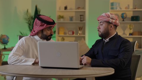 متابعة إستراتيجيات وأهداف الشركة, اجتماع في المكتب لمناقشة سير العمل, دراسة وتحليل المشاريع الجديدة, موظفان عربيان خليجيان سعوديان  يستخدمون جهاز اللابتوب المحمول، استخدام التقنيات الحديثة، مناقشة ومتابعة الاعمال، التعاون والتفاهم بين الموظفين، مهن ووظائف مكتبية