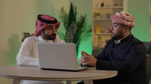 اجتماع في المكتب لمناقشة سير العمل, متابعة إستراتيجيات وأهداف الشركة, دراسة وتحليل المشاريع الجديدة, موظفان عربيان خليجيان سعوديان  يستخدمون جهاز اللابتوب المحمول، استخدام التقنيات الحديثة، مناقشة ومتابعة الاعمال، التعاون والتفاهم بين الموظفين، مهن ووظائف مكتبية