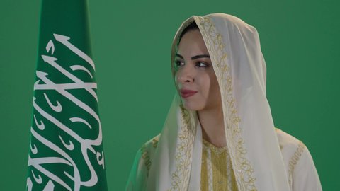 تأسيس الدولة السعودية الأولى 22 فبراير، ذكرى يوم بدينا 1727 م، ارتداء الزي السعودي التقليدي الشعبي , بورتريه لإمرأة عربية خليجية سعودية ترتدي الثوب الابيض المطرز بالذهبي وتضع الشيله على رأسها تنظر الى العلم بتعابير الفخر والاعتزاز, كروما ، خلفية خضراء