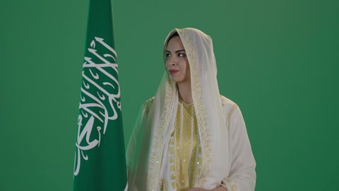 ذكرى يوم بدينا 1727 م، تأسيس الدولة السعودية الأولى 22 فبراير، ارتداء الزي السعودي التقليدي الشعبي , بورتريه لإمرأة عربية خليجية سعودية ترتدي الثوب الابيض المطرز بالذهبي وتضع الشيله على رأسها تنظر الى العلم بتعابير الفخر والاعتزاز, كروما ، خلفية خضراء