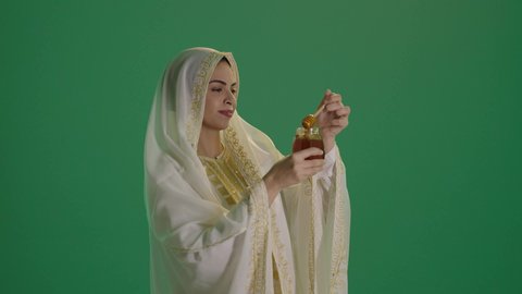 غذاء صحي مفيد ، استخراج عسل النحل الطبيعي من المناحل، منتج غذائي محلي وطني في المملكة العربية السعودية،  ارتداء الزي السعودي التقليدي الشعبي ,بورتريه لإمرأة عربية خليجية سعودية ترتدي الثوب الابيض المطرز بالذهبي وتضع الشيله على رأسها تحمل بيدها وعاء زجاجي ملئ بالعسل ، كروما ، خلفية خضراء