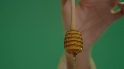 A local national food product in the Kingdom of Saudi Arabia, extracting natural honey from beehives, wearing traditional Saudi folk attire, healthy beneficial foods, a portrait of an Arab Gulf Saudi woman wearing a white dress embroidered with gold and wearing a shayla on her head, holding a glass container filled with honey in her hand, chroma, green background.