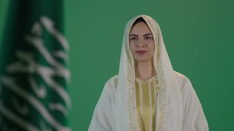 ذكرى يوم بدينا 1727 م، تأسيس الدولة السعودية الأولى 22 فبراير، ارتداء الزي السعودي التقليدي الشعبي , بورتريه لإمرأة عربية خليجية سعودية ترتدي الثوب الابيض المطرز بالذهبي وتضع الشيله على رأسها تنظر الى العلم بتعابير الفخر والاعتزاز, كروما ، خلفية خضراء