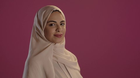 تعابير البهجة والسرور، الأناقة و الاهتمام بالمظهر الخارجي, مفهوم الأنوثة و النعومة, بورتريه لامرأة عربية خليجية سعودية ترتدي العباءة والحجاب تنظر الى الكاميرا بايماءات السعادة ،خلفية حمراء