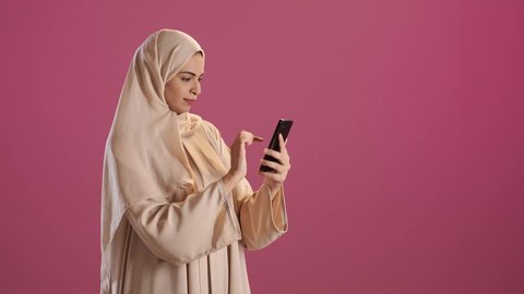 دمج التكنولوجيا فى الحياه اليوميه ، تصفح التطبيقات وبرامج التواصل الاجتماعي، تبادل الأحاديث مع الأهل والأصدقاء، بورتريه لامرأة عربية خليجية سعودية ترتدي العباءة والحجاب تمسك بيدها الجوال ، استخدام الأجهزة والتقنيات الحديثة المتطورة، خلفية حمراء