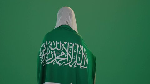 ذكرى يوم بدينا 1727 م، تأسيس الدولة السعودية الأولى 22 فبراير، ارتداء الزي السعودي التقليدي الشعبي , بورتريه من الخلف لإمرأة عربية خليجية سعودية ترتدي الثوب الابيض المطرز بالذهبي وتضع الشيله على رأسها تمسك راية وشعار يوم التأسيس بتعابير الفخر والاعتزاز, كروما ، خلفية خضراء