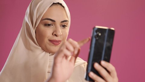 تصفح التطبيقات وبرامج التواصل الاجتماعي، تبادل الأحاديث مع الأهل والأصدقاء، بورتريه لامرأة عربية خليجية سعودية ترتدي العباءة والحجاب تمسك بيدها الجوال ، استخدام الأجهزة والتقنيات الحديثة المتطورة، خلفية حمراء