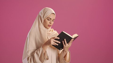 مفهوم حب المطالعه ، قراءة الكتب بتمعن ، بورتريه لامرأة عربية خليجية سعودية ترتدي العباءة والحجاب تحمل بيدها كتاب تثقيفي ، إيماءات التركيز والاندماج ، الاستمتاع بقراءة الروايات والقصص ، خلفية حمراء