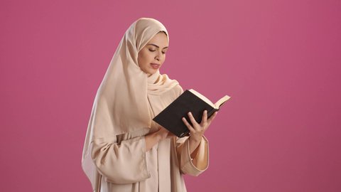 The culture of self-learning, reading books attentively, a portrait of a Saudi Gulf Arab woman wearing an abaya and hijab holding an educational book in her hand, gestures of focus and engagement, enjoying reading novels and stories, red background.