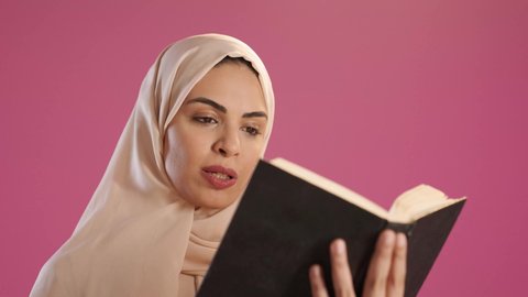 The culture of self-learning, reading books attentively, a portrait of a Saudi Gulf Arab woman wearing an abaya and hijab holding an educational book in her hand, gestures of focus and engagement, enjoying reading novels and stories, red background.