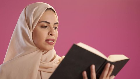 The culture of self-learning, reading books attentively, a portrait of a Saudi Gulf Arab woman wearing an abaya and hijab holding an educational book in her hand, gestures of focus and engagement, enjoying reading novels and stories, red background.