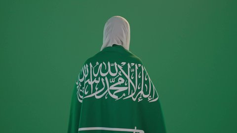 ذكرى يوم بدينا 1727 م، تأسيس الدولة السعودية الأولى 22 فبراير، ارتداء الزي السعودي التقليدي الشعبي , بورتريه من الخلف لإمرأة عربية خليجية سعودية ترتدي الثوب الابيض المطرز بالذهبي وتضع الشيله على رأسها تمسك راية وشعار يوم التأسيس بتعابير الفخر والاعتزاز, كروما ، خلفية خضراء