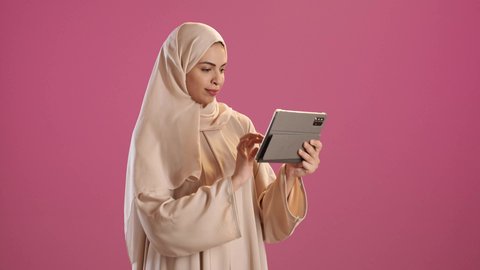 ايماءات السرور والبهجة, الدردشة و التواصل الاجتماعي, إجراء مكالمة فيديو عبر التابلت,بورتريه لامرأة عربية خليجية سعودية ترتدي العباءة والحجاب تنظر الى الكاميرا بايماءات السعادة , تقنيات العمل عن بعد ، خلفية حمراء