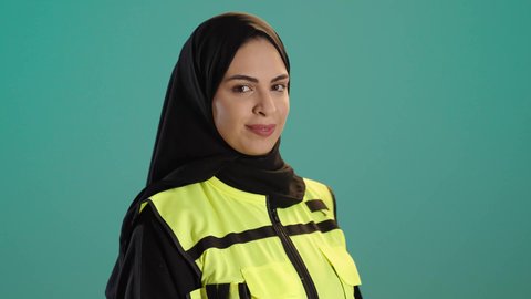 ادارة المشاريع الهندسية, بورتريه لمهندسة معمارية عربية خليجية امارتية ترتدي خوذة وسترة الحماية تقف بتعابير البهجة والسعادة، شابة سعودية تنظر الكاميرا بايماءات السرور تعمل في القطاع الهندسي، كروما ، خلفية خضراء