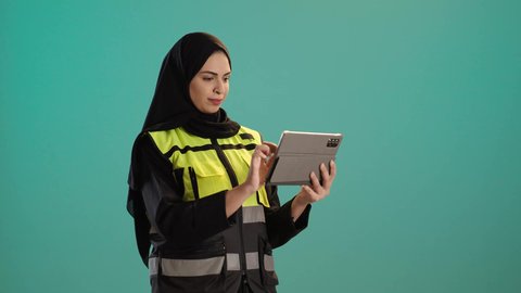A portrait of an Emirati Gulf Arab engineer wearing a jacket and safety helmet working on a tablet, a young Saudi woman supervising the work, studying the fundamentals of the project, integrating modern technologies in engineering, working in the engineering sector, managing engineering projects, chroma, green background.
