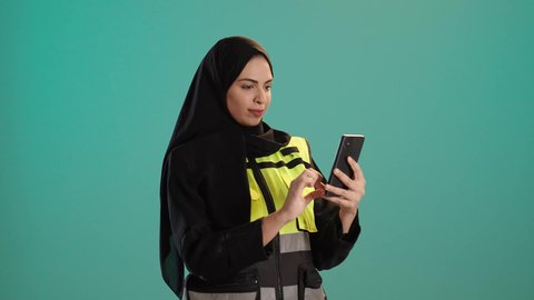 وظائف ومهن نسائية, دمج التكنولوجيا الحديثة بالمجال الهندسي،العمل في القطاع الهندسي, بورتريه لمهندسة عربية خليجية امارتية ترتدي خوذة وسترة الحماية تقوم باجراء مكالمة فيديو، شابة سعودية تحمل بيدها الهاتف المحمول، كروما ، خلفية خضراء