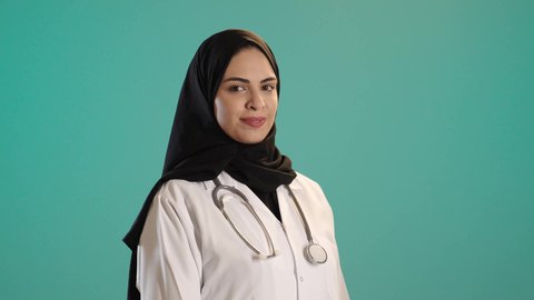 العمل في القطاع الصحي في المملكة، مفهوم الطب والرعاية الصحية، بورتريه لطبيبة عربية خليجية سعودية ترتدي العباءة والحجاب مع المعطف الابيض تقف باستقامة، النظر بايماءات السعادة والسرور، مهن ووظائف نسائية، تقديم الخدمات للمرضى بكل كفاءه، كروما ، خلفيه خضراء