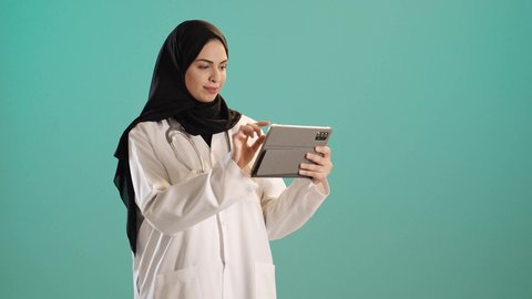 استخدام التكنولوجيا في البحث والتطوير، تقديم الخدمات للمرضى بكل كفاءه،اجراء الاستشارات الطبيه عن بعد، بورتريه لطبيبة عربية خليجية سعودية ترتدي العباءة والحجاب مع المعطف الابيض تعمل على التابلت، مهن ووظائف صحية، كروما ، خلفيه خضراء