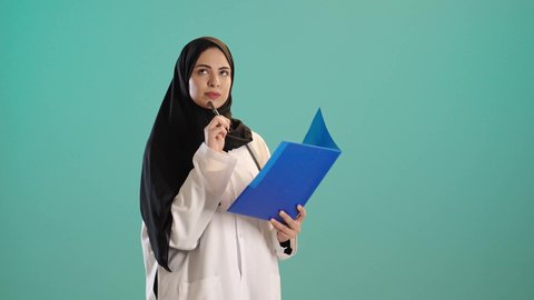 بورتريه لطبيبة عربية خليجية سعودية ترتدي العباءة والحجاب مع المعطف الابيض تضع السماعات الطبيه حول رقبتها، تحمل بيدها أوراق وملفات المرضى، العمل في القطاع الصحي في المملكة العربية السعودية، تقديم الرعاية الصحية للمرضى، كتابة التقارير الطبية ، كروما ، خلفيه خضراء