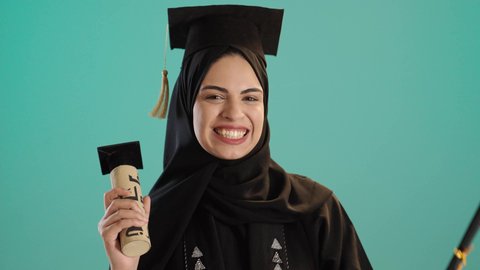 الاحتفال بإنهاء الدراسة الجامعية، الشعور بالفخر والثقة بالنفس، مفهوم الاجتهاد والتفوق، بورتريه لشابة عربية خليجية سعودية ترتدي العباءه والحجاب وقبعة التخرج تحمل الشهادة بإيماءات الرضا والسرور ، كروما ، خلفية خضراء