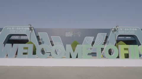 Welcoming model for visitors to the FII exhibition, discussing the global economic future, major investors, a global conference to discuss the future of technology and investment, how to invest in the global future and education, artificial intelligence, technology and sustainable energy, and Saudi Arabia's Vision 2030.