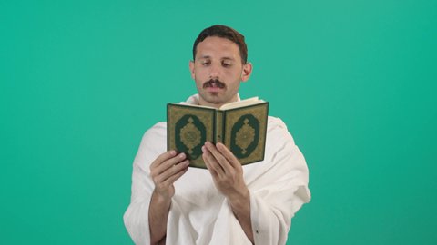 مفهوم العبادة والطاعة والتقرب الى الله في شهر رمضان المبارك, التمعن بسور القرآن الكريم, تدبر الآيات القرآنية والتفكر بها، رجل عربي خليجي سعودي يرتدي لباس الاحرام يقرأ من المصحف الشريف، خلفية خضراء ، كروما