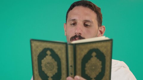 التمعن بسور القرآن الكريم, مفهوم العبادة والطاعة والتقرب الى الله في شهر رمضان المبارك, تدبر الآيات القرآنية والتفكر بها، رجل عربي خليجي سعودي يرتدي لباس الاحرام يقرأ من المصحف الشريف، خلفية خضراء ، كروما