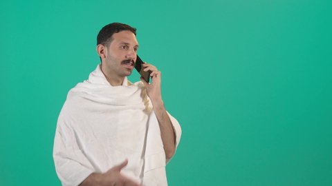 الدردشة مع الأهل والأصدقاء، استخدام جهاز تقني حديث، رجل عربي خليجي سعودي يرتدي لباس الاحرام يمسك بيده الهاتف المحمول، دمج التقنية والتكنولوجيا بالحياة اليومية، تصفح مواقع التواصل الاجتماعي، خلفية خضراء ، كروما