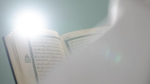 Reflecting on the verses of the Holy Quran, the concept of worship, obedience, and drawing closer to God during the blessed month of Ramadan, contemplating the Quranic verses and thinking about them, an Arab Gulf Saudi man wearing the Ihram clothing reading from the Holy Mushaf, green background, chroma.