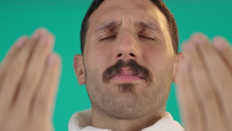 مفهوم أركان الإسلام، الدعاء و التضرع لرب العباد,اداء مناسك الحج والعمرة، العبادة والتقرب الى الله، رجل عربي خليجي سعودي يرتدي لباس الاحرام يرفع يديه بايماءات الدعاء ،الطاعة والتقرب الى الله، خلفية خضراء ، كروما