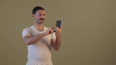 Chatting with family and friends, using a modern technological device, an Arab Gulf Saudi man wearing pants and a white t-shirt holding a mobile phone in his hand, integrating technology and technology into daily life, browsing social media.